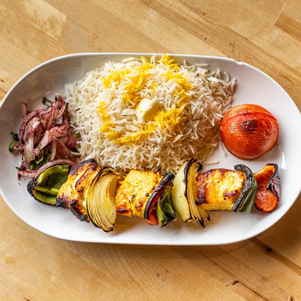 Grilled paneer and vegetable skewer with rice, roasted tomato, and red onion salad on a white plate.