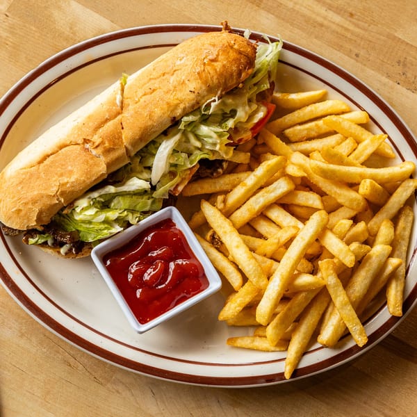 Italiamo Kitchen's cheesesteak sub with lettuce, tomatoes, and onions, served with fries and ketchup.