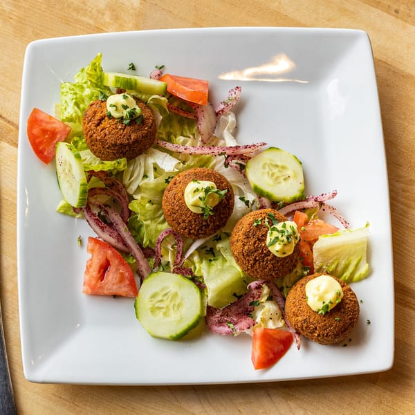 Falafel salad with lettuce, tomatoes, cucumbers, red onions, and a dollop of sauce on a white plate.