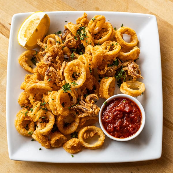 Crispy fried calamari with marinara sauce and a lemon wedge on a white plate.